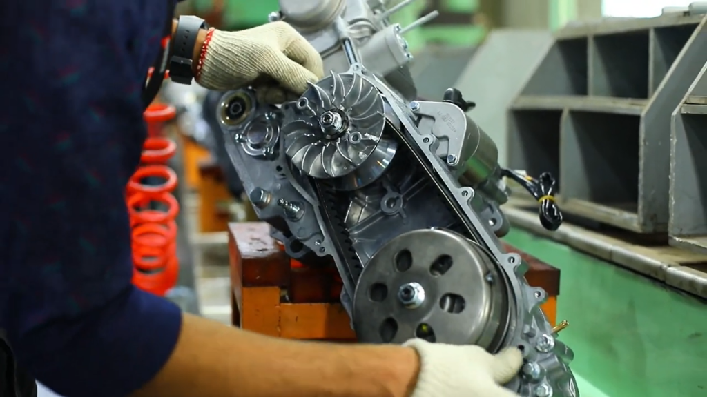 Everyone Blames China... But India Just Took 1 in 3 New Cars in Mzansi A mechanic in protective gloves carefully fits a gasket onto an engine block between two pulleys inside a factory, highlighting the precision and skill involved in automotive manufacturing.