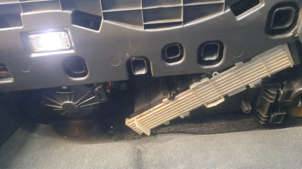 Clear view of the white plastic cabin filter housing cover located under the dashboard of an Audi A4 B8, exposed after removing the protective foam trim.